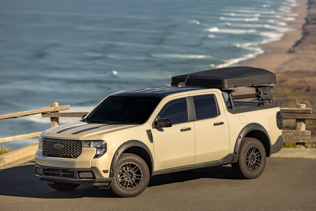 Tan pickup truck with rooftop tent set up near the ocean, ready for a night of camping