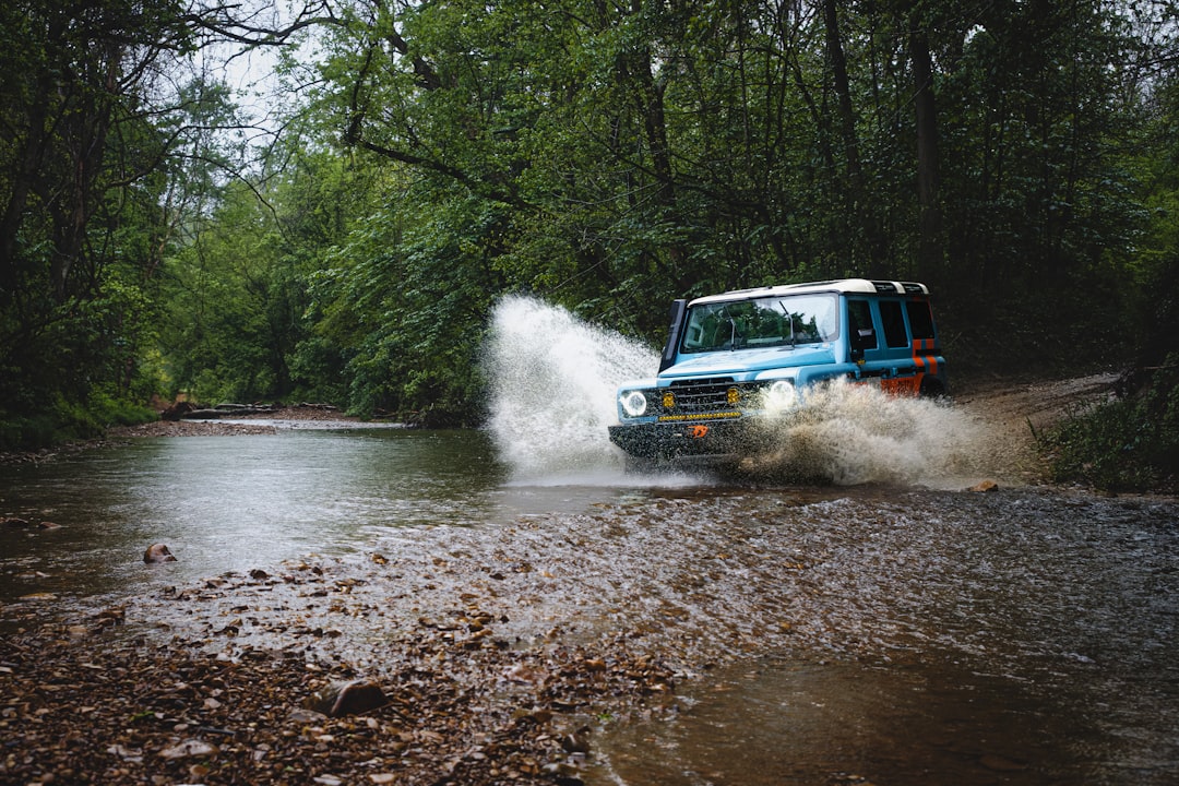 A 4x4 vehicle crossing a shallow stream on a dirt trail, water splashing around the tires