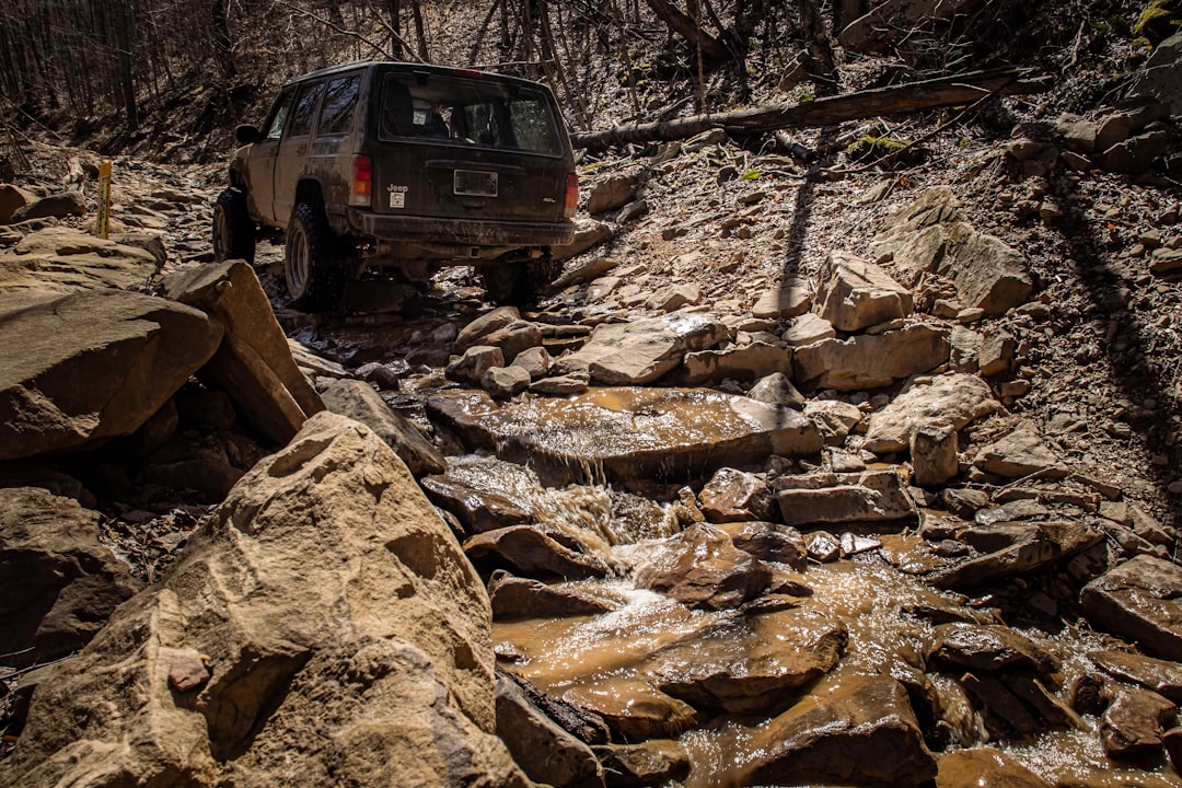 A Jeep driving through a rocky creek in the woods