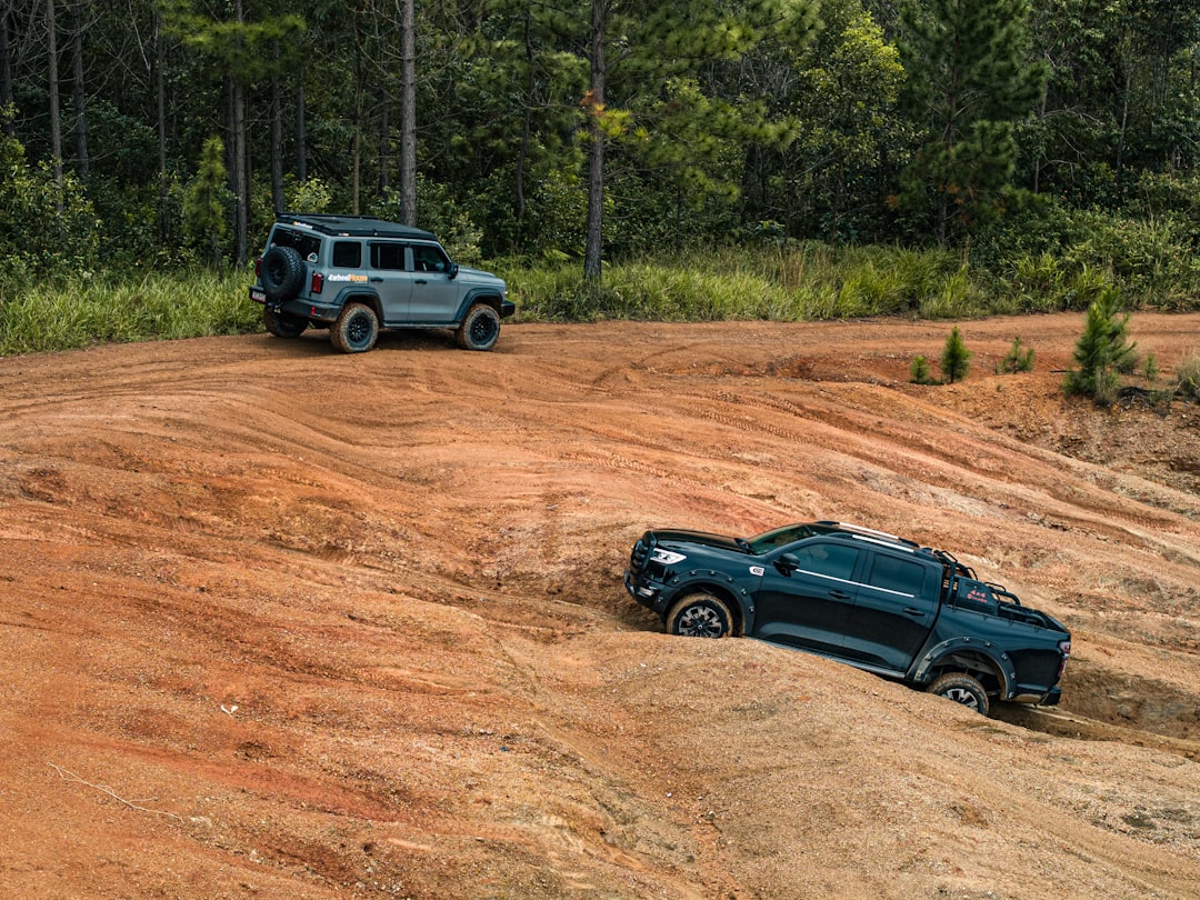 Two modified 4WD vehicles crossing sandy uneven terrain in a dense forest setting